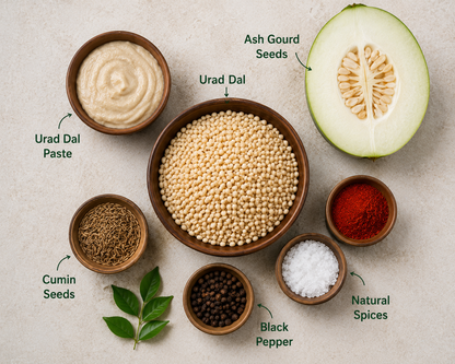 Ingredients for a recipe including Urad Dal, Ash Gourd, Urad Dal Paste, Cumin Seeds, Black Pepper, and Natural Spices on a neutral background.