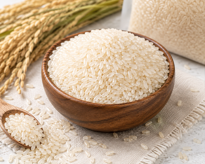 Unpolished white rice grains piled in a wooden bowl, with a small wooden spoon holding some rice.