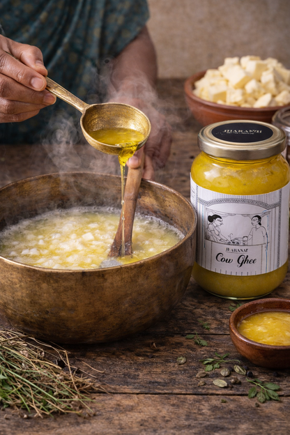 Person ladling ghee into a pot with a jar of cow ghee labeled 'jharani' in the background.