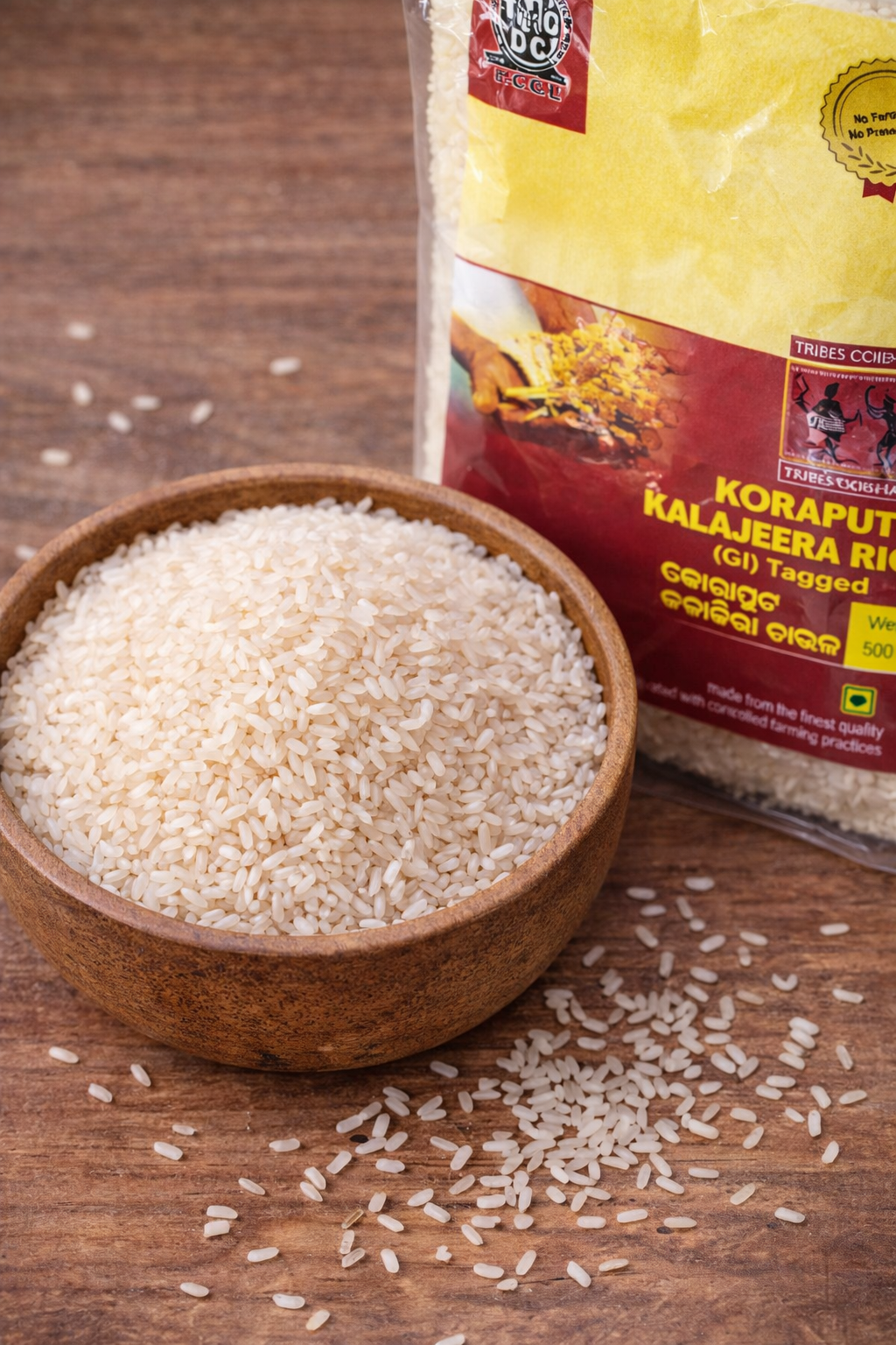Wooden bowl of rice with a package of Koraput Kalajeera Rice on a wooden surface