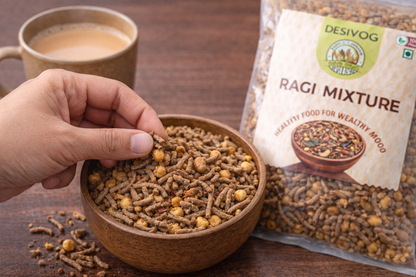 Hand holding a bowl of Ragi mixture with a package and cup of tea on a wooden surface