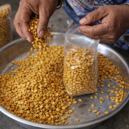Person packaging yellow lentils into a clear plastic bag on a metal tray.