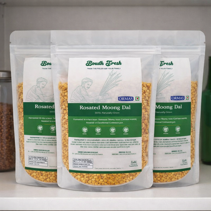 Three packages of Ormas Rosated Moong Dal on a white surface with a blurred background.