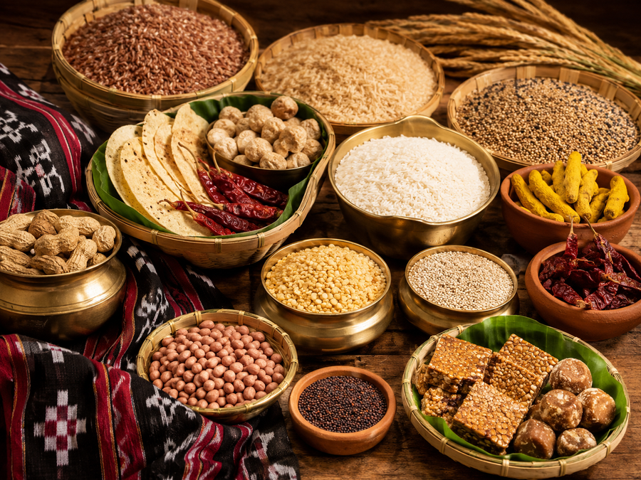 Assorted grains, legumes, and snacks in bowls on a wooden surface with traditional fabric.
