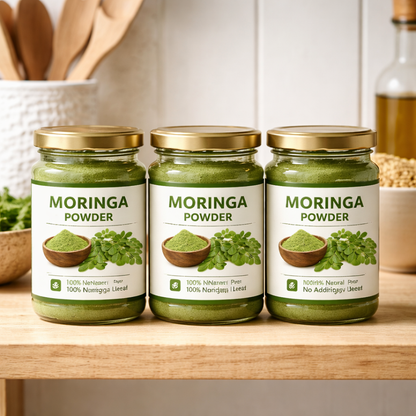 Three jars of Moringa Powder on a wooden shelf with kitchen utensils in the background.