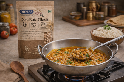Pot of chickpea curry with a spoon, Ormas Desi Buta (Tiasi) package in the background.