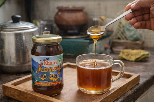Khaini Honey jar with a spoon drizzling honey into a glass of tea on a wooden tray.