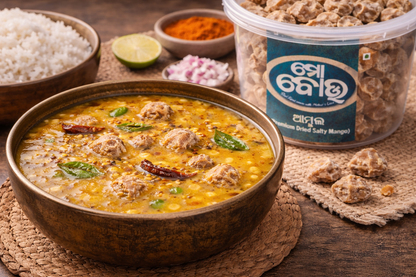 Bowl of curry with meatballs, rice, and a container of dried mangoes on a wooden surface.